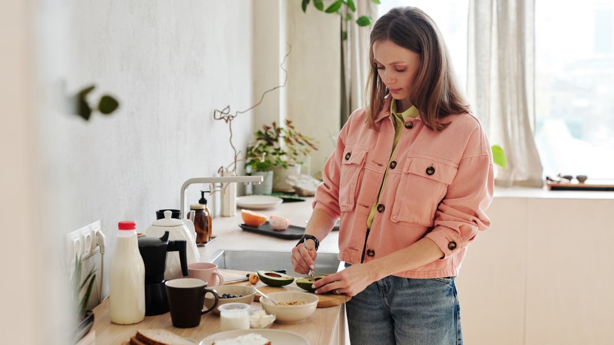 A woman slices an avocado in a bright, modern kitchen with natural light.