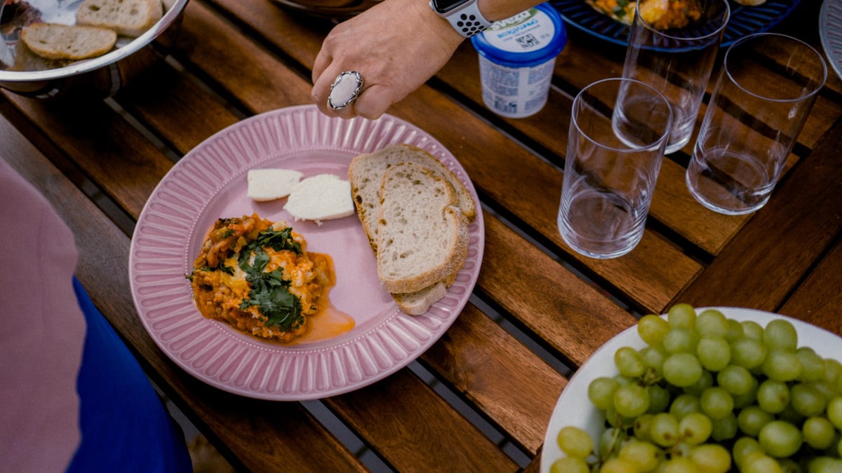 A casual outdoor dining table with bread, greens, and a side dish for brunch.
